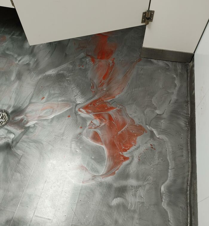 Unfortunate interior design with a textured floor resembling messy paint spills near cabinet in a public space.