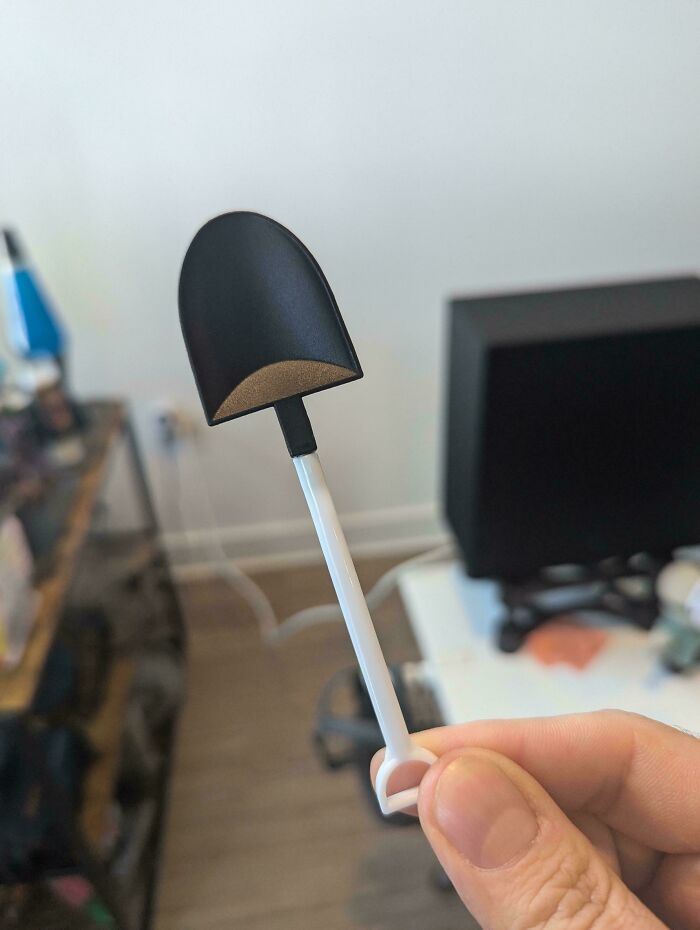 A small, black spoon with a surprise hollow scoop, held up indoors.