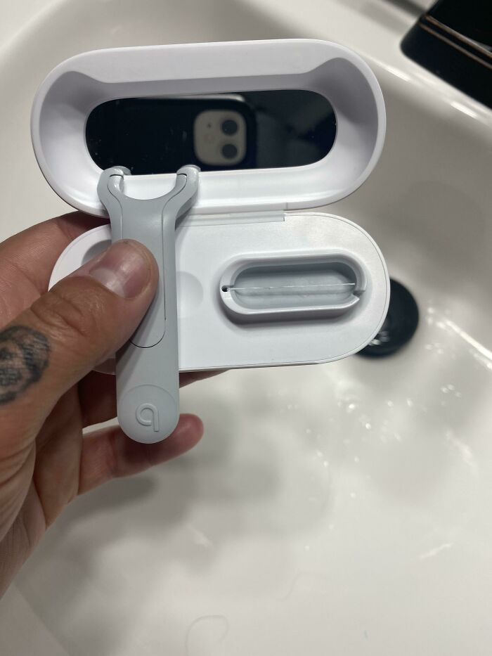 Cool product: a compact razor with a case, featuring an unexpected mirror inside, held by a tattooed hand over a sink.