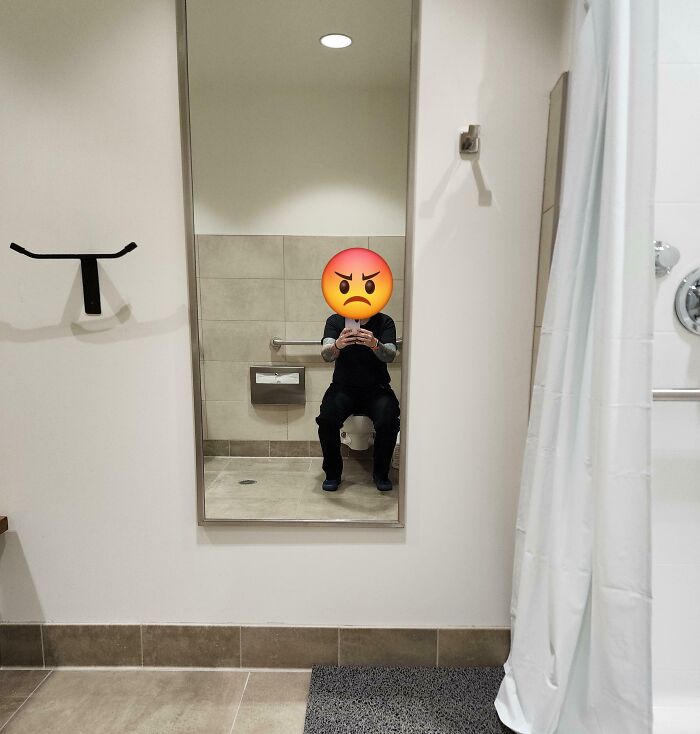 Unfortunate public interior design with a bathroom mirror reflecting a person on the toilet.