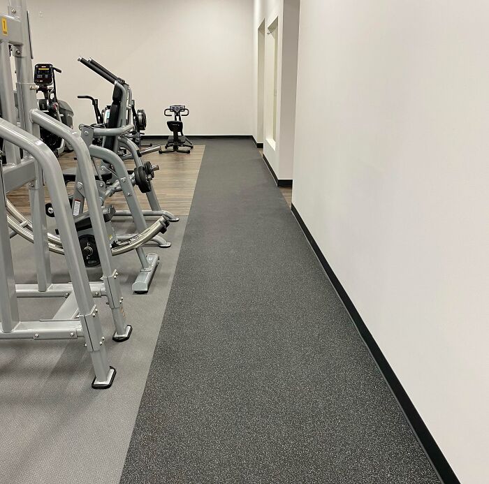 Gym with unfortunate public interior design; narrow walkway between exercise machines and a wall.