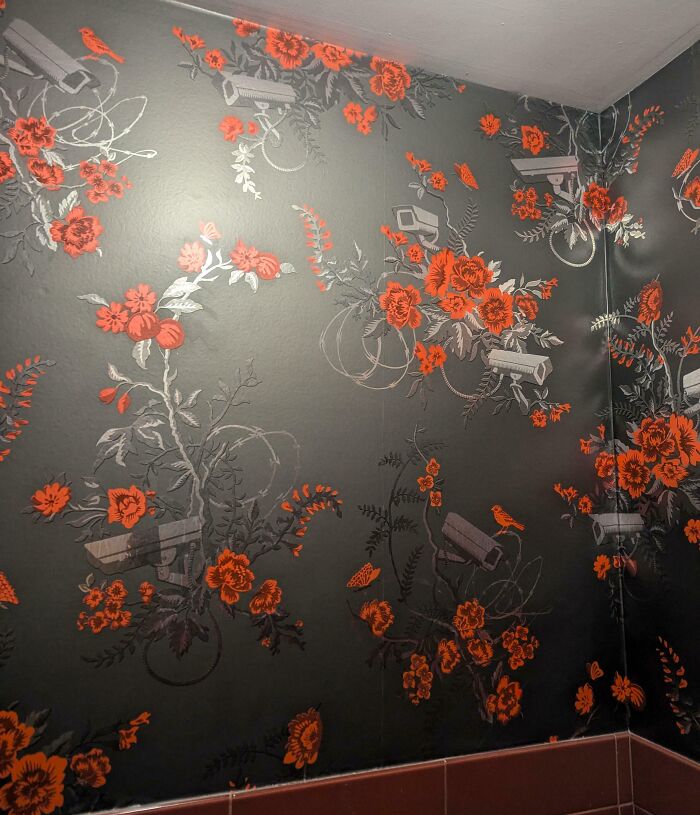 Floral wallpaper featuring red flowers and security cameras, showcasing unfortunate public interior design.