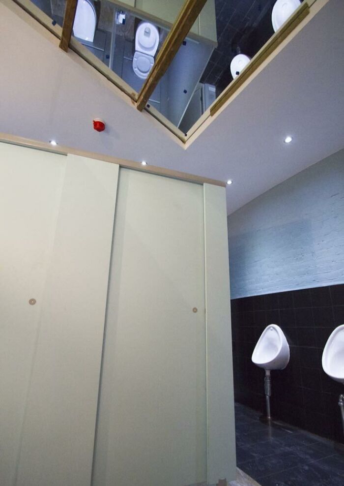 Unfortunate public interior design showing restroom with mirrors on the ceiling reflecting toilets and urinals.