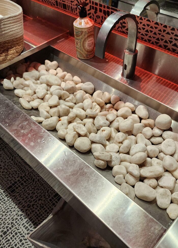 Stainless steel sink filled with white rocks, showcasing unfortunate interior design choices in a public space.