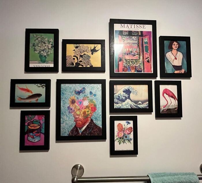 Gallery of vibrant artwork in black frames, reflecting dopamine decor style on a white wall above a towel rack.