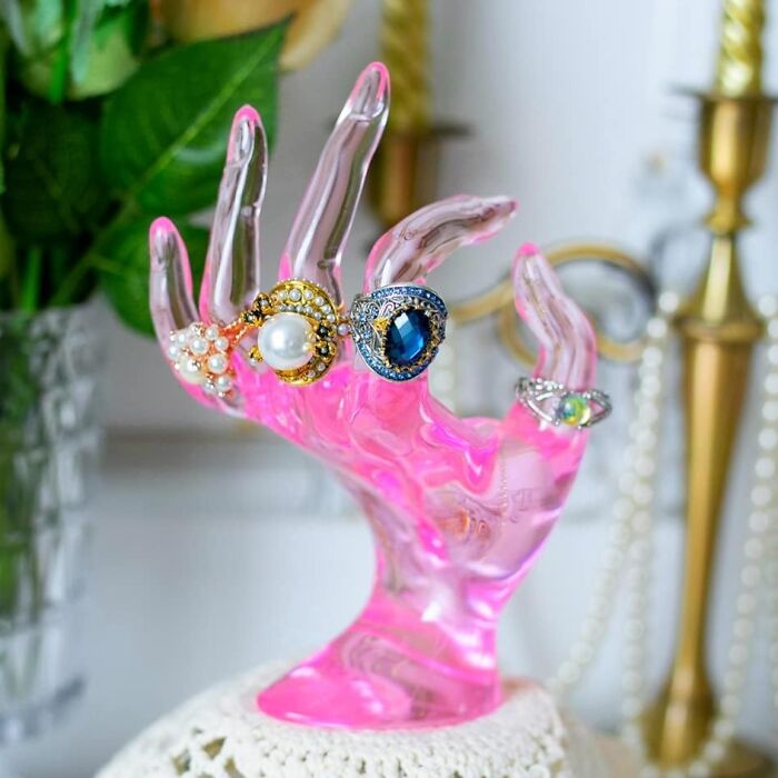 Pink glass hand display with rings, embodying Dopamine Decor style against a decorative background.