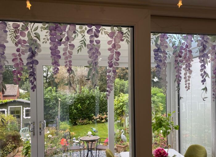 Purple wisteria decor hanging inside a glass door overlooking a lush garden.