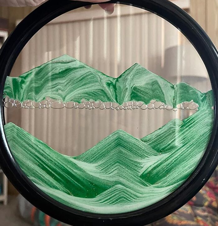 Decorative sand art piece with green mountains creating a calming Dopamine Decor effect in a circular frame.