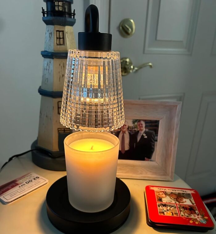 Cozy dopamine decor with a lit candle under a glass fixture on a bedside table, creating a warm ambience.