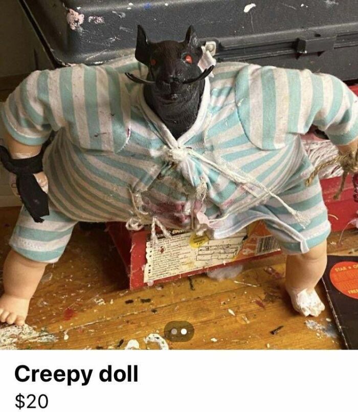 Creepy doll with a dark animal head, striped clothes, sitting on a wooden surface.