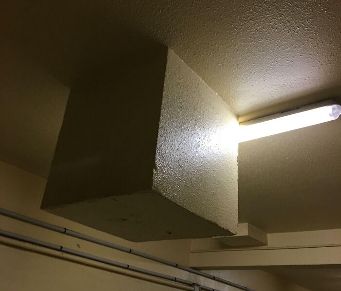 Awkward interior design with a protruding ceiling block nearly touching a fluorescent light fixture.