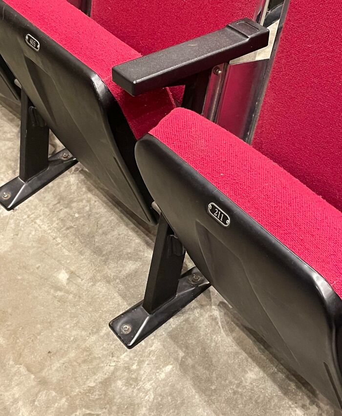 Unfortunate interior design featuring misaligned theater seats with red upholstery and black armrests.