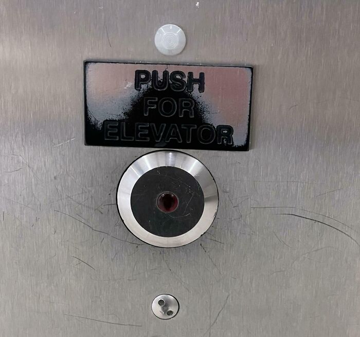 Elevator button misaligned under sign, an example of unfortunate interior design.