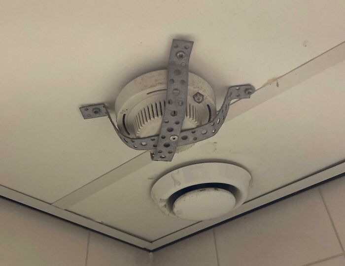 Ceiling with unfortunate interior design showing awkwardly installed smoke detector with metal straps.