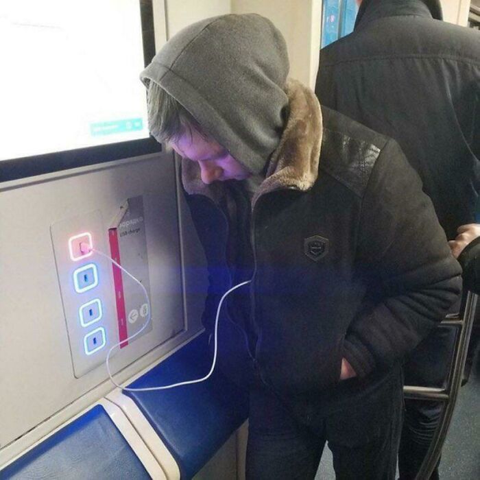 Passenger humorously charging phone on subway.