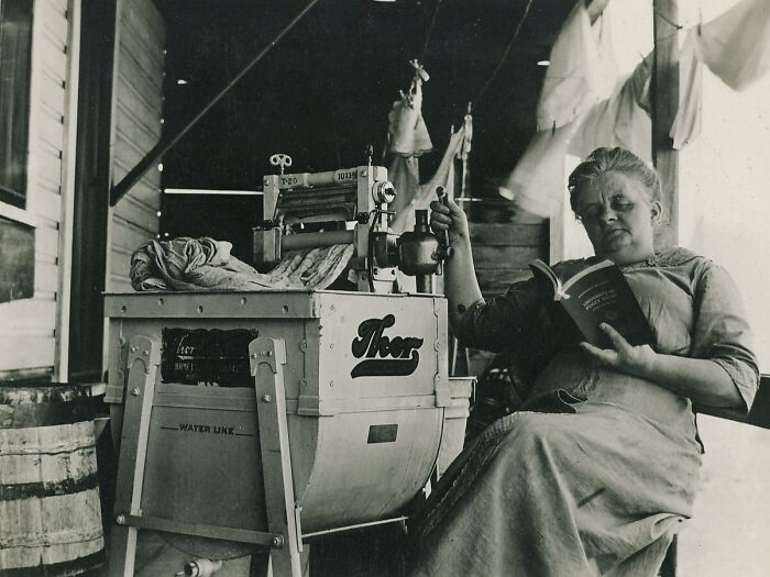 Woman reading beside an early washing machine, illustrating historical inventions ahead of their time.