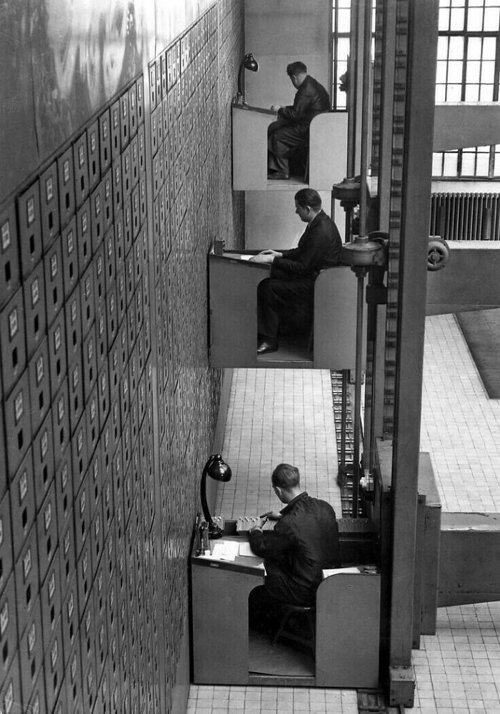 Workers in elevated desks managing files, showcasing historical inventions that were ahead of their time.