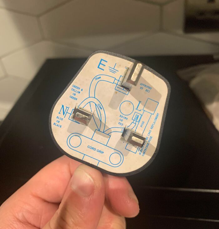 Person holding a UK plug with wiring diagram, showcasing cool products with surprises.