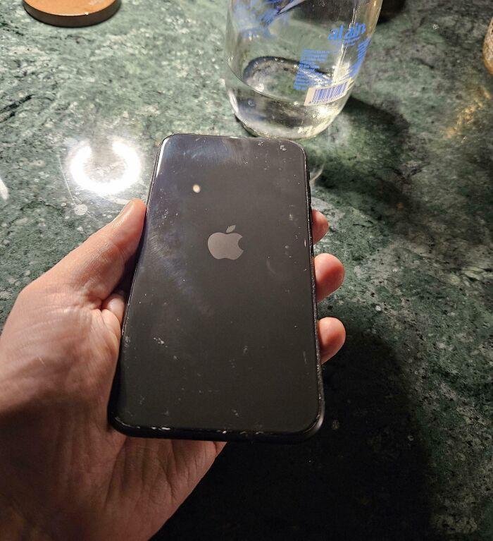 A black iPhone with visible scratches on a green marble surface, part of cool products with surprises.