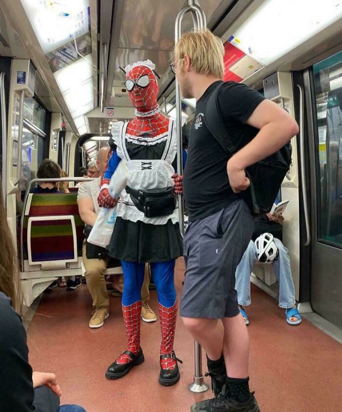 Passenger in Spiderman costume with maid outfit on subway, creating a funny train scene.