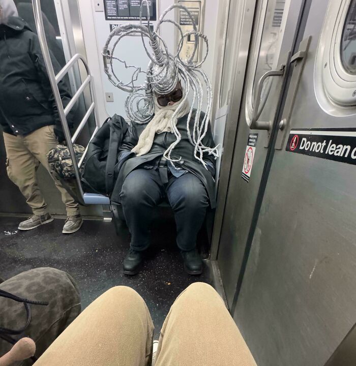 Passenger on subway with a quirky wire hat, creating a funny scene during the train ride.