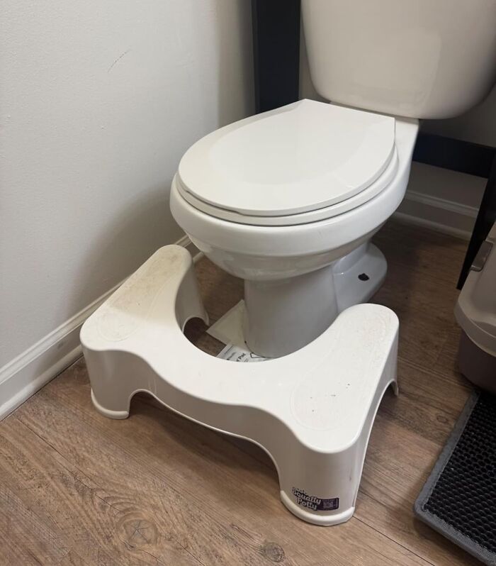 Toilet with footstool on wooden floor, addressing body issues in bathroom posture.