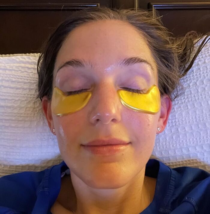 Woman relaxing with under-eye patches addressing body issues, lying on a bed.