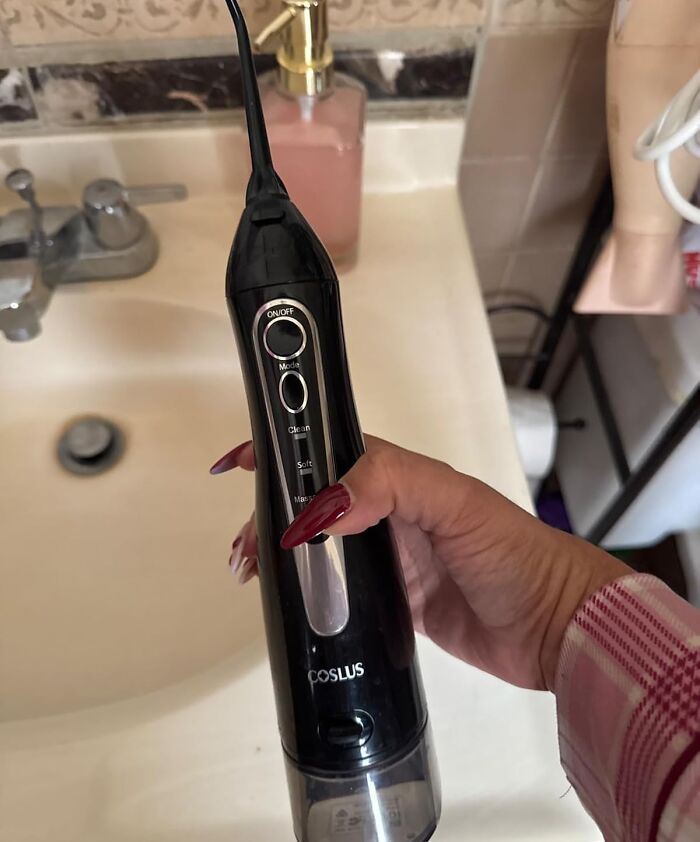 A person holding a black oral irrigator near a bathroom sink, highlighting body hygiene concerns.