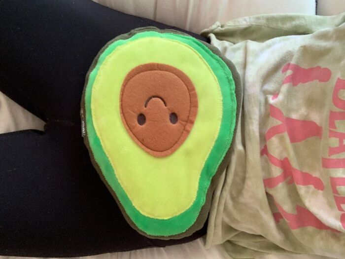 Avocado cushion resting on someone's lap, illustrating unavoidable body issues humorously.