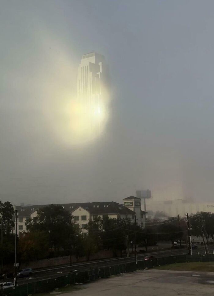 Confusing perspective creates an illusion of a building floating above mist-covered houses and trees.