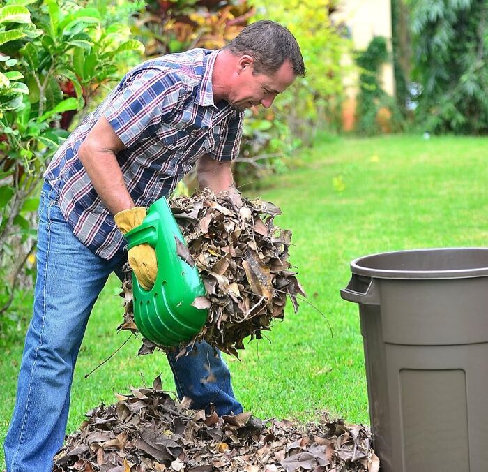 Man using a genius leaf scooping tool to collect leaves into a bin.