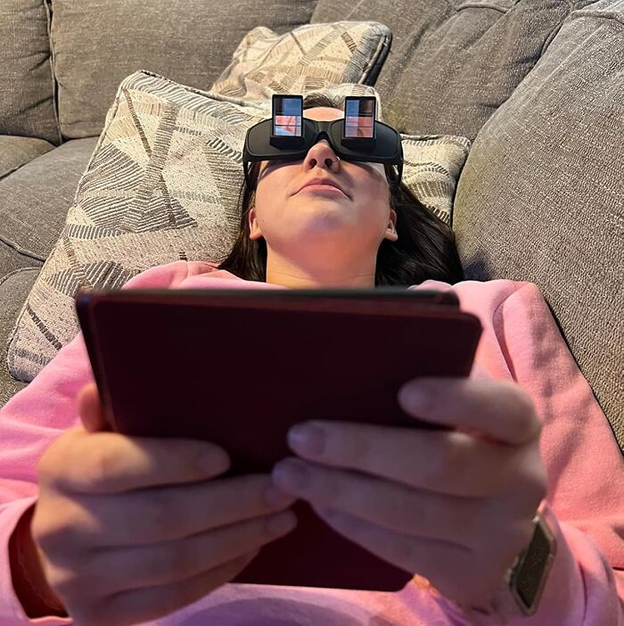 Person using prism glasses while reading on a couch, highlighting a borderline genius gadget.