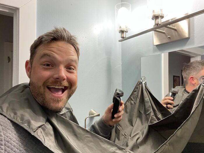 Man happily using a grooming cape and clipper in the bathroom, demonstrating a borderline genius grooming tool.