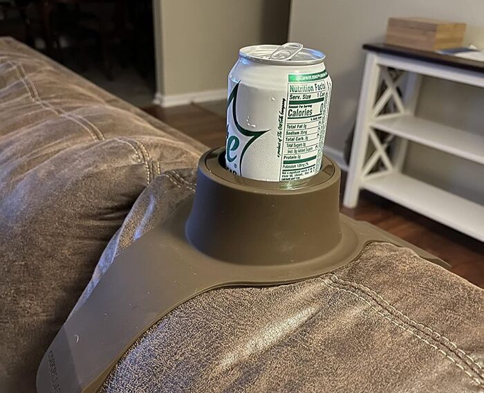 Couch cup holder genius, holding a soda can on a brown sofa armrest in a living room setting.