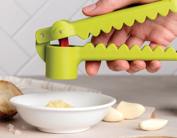 A green garlic press crushing cloves into a bowl, showcasing a borderline genius kitchen tool.