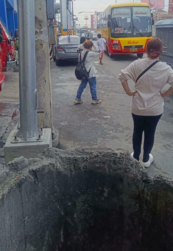 Confusing perspective photo showing people on a street with an unexpected large hole in the foreground.