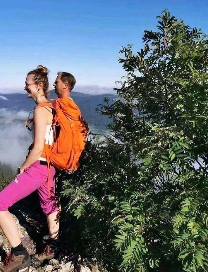 Confusing perspective image of two hikers, one appearing to wear the other as a backpack, in a scenic outdoor setting.