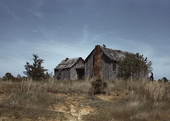 Old wooden house on a grassy hill under a clear sky, captured in 1940 color photos.