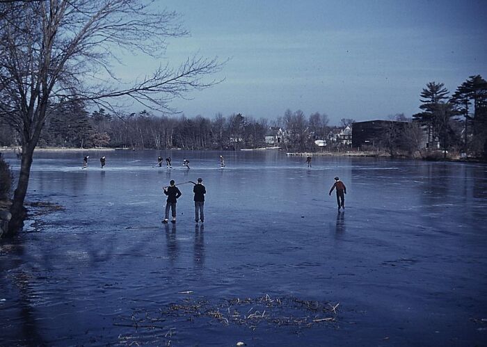 People skating on a frozen lake in a 1940 color photo, surrounded by trees and distant buildings.