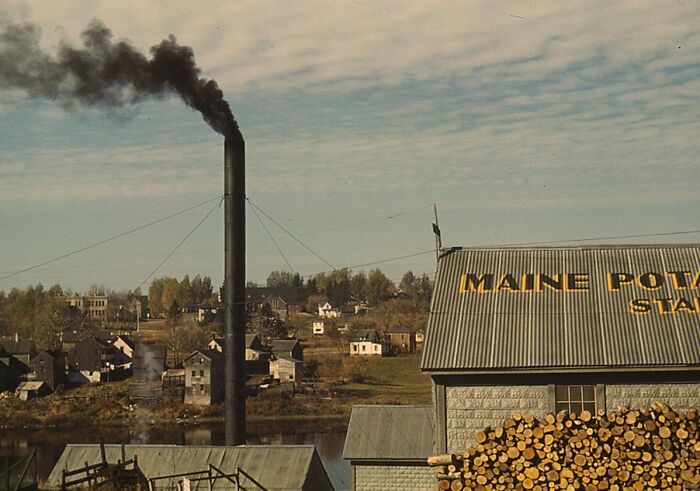 1940 color photo of a smokestack in a rural town with a building labeled "Maine Potato."