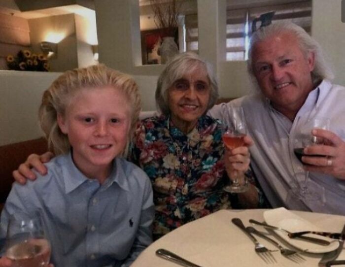 Family with unique hairstyles smiling and holding wine glasses at a restaurant.