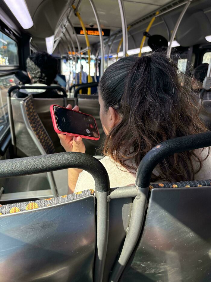 Person on a bus holding a loud phone conversation on speaker, ignoring other passengers, displaying inconsiderate behavior.