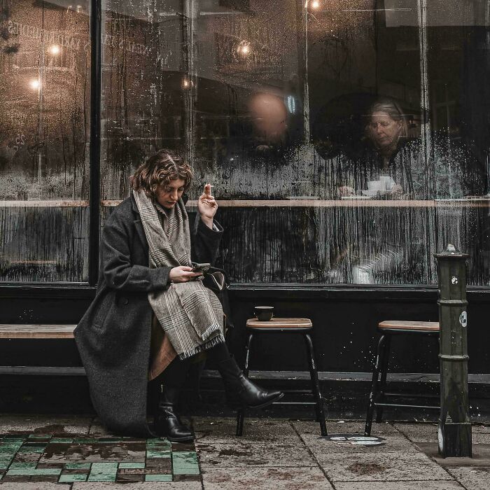 Person sitting outside a cafe, holding a smartphone and smoking, resembling a scene from a Renaissance painting.