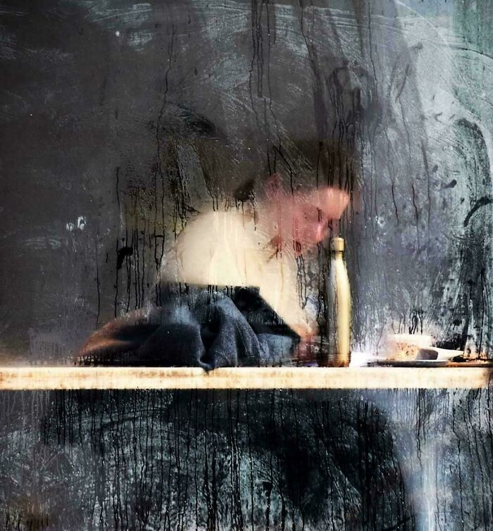 A rain-streaked window with a person behind, resembling a Renaissance painting scene.