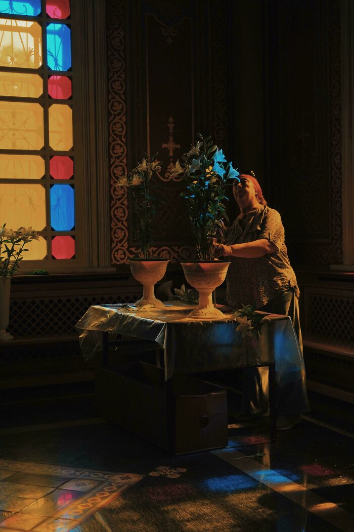 Person arranging flowers in a room with stained glass, resembling a Renaissance painting.