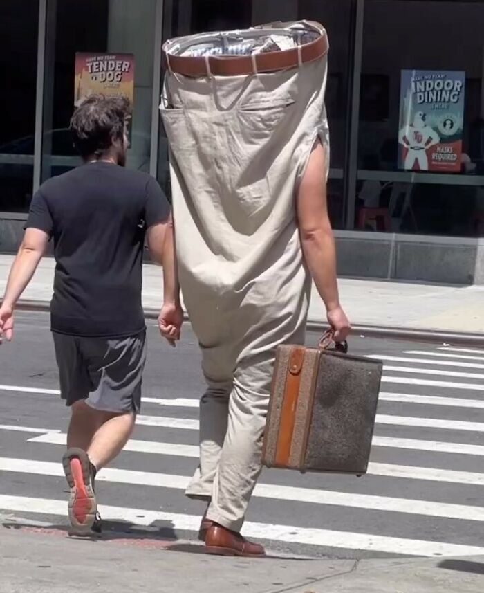 NYC local wearing an oversized pants costume with a suitcase, showcasing experimental fashion on a city street.