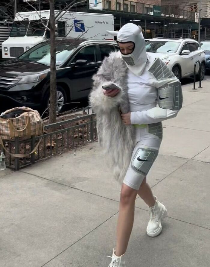 New York local in futuristic attire with a fur accent, walking while checking phone, showcasing experimental fashion.