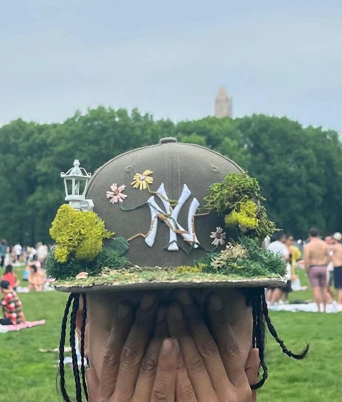 NYC local wearing a creatively decorated cap with floral and greenery elements in a park setting.