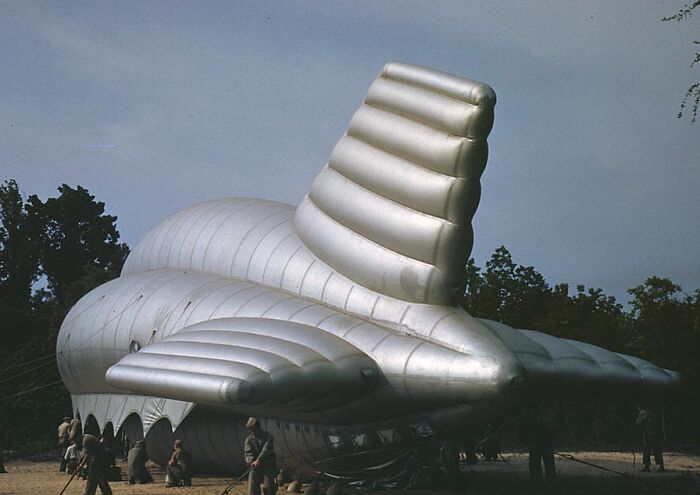 Inflatable military decoy resembling a tank in 1940 color photo, with soldiers setting it up in a wooded area.