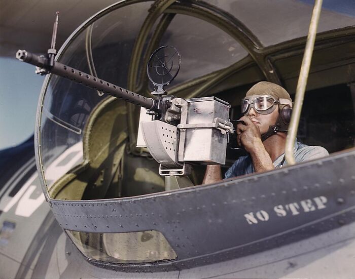 World War II gunner operating a turret in 1940 color photo, wearing goggles and a headset in a combat aircraft.